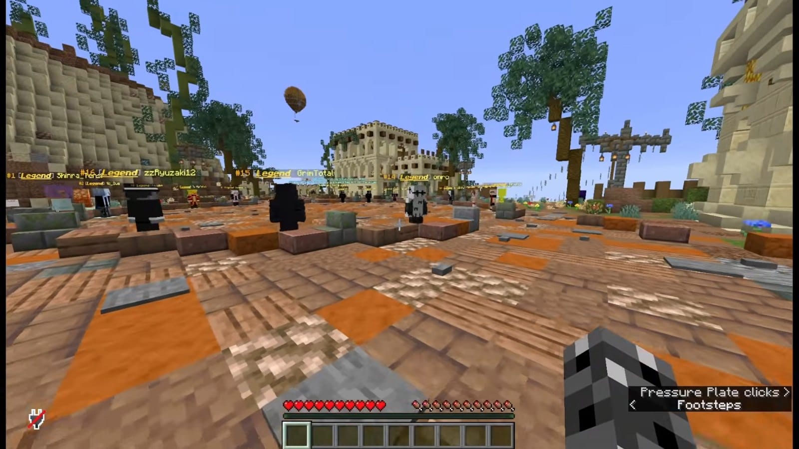 Players standing on the brown and orange plaza of 6b6t's lobby, between sandstone buildings and trees, with a hot air balloon overhead.