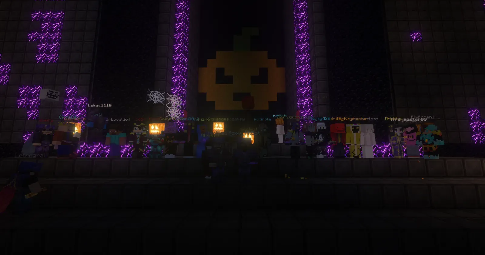 A large group of players standing in front of a giant pixel-art pumpkin face between walls of glowing purple blocks