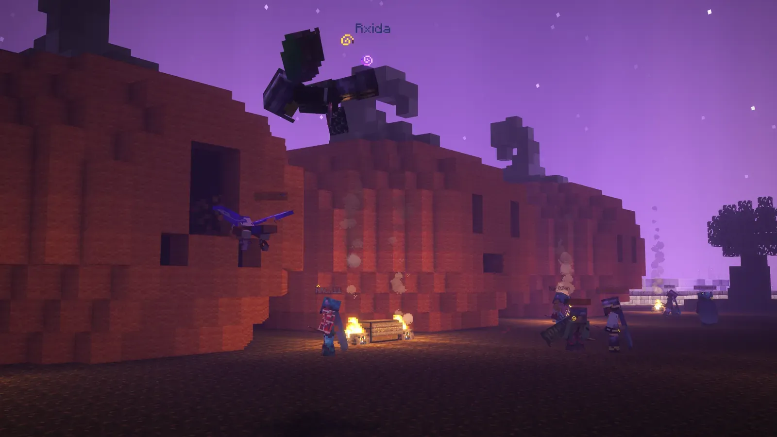 Players around a campfire in front of a giant carved pumpkin build under a purple night sky
